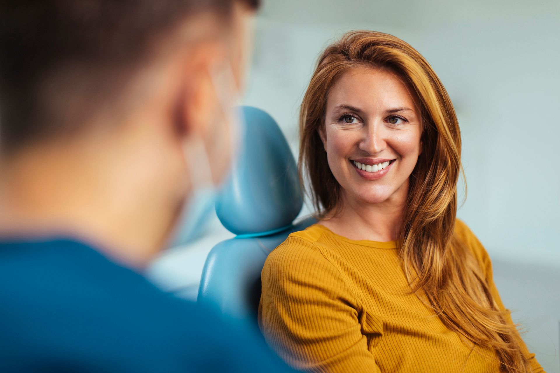 A woman is smiling while sitting in a dental chair talking to a dentist.