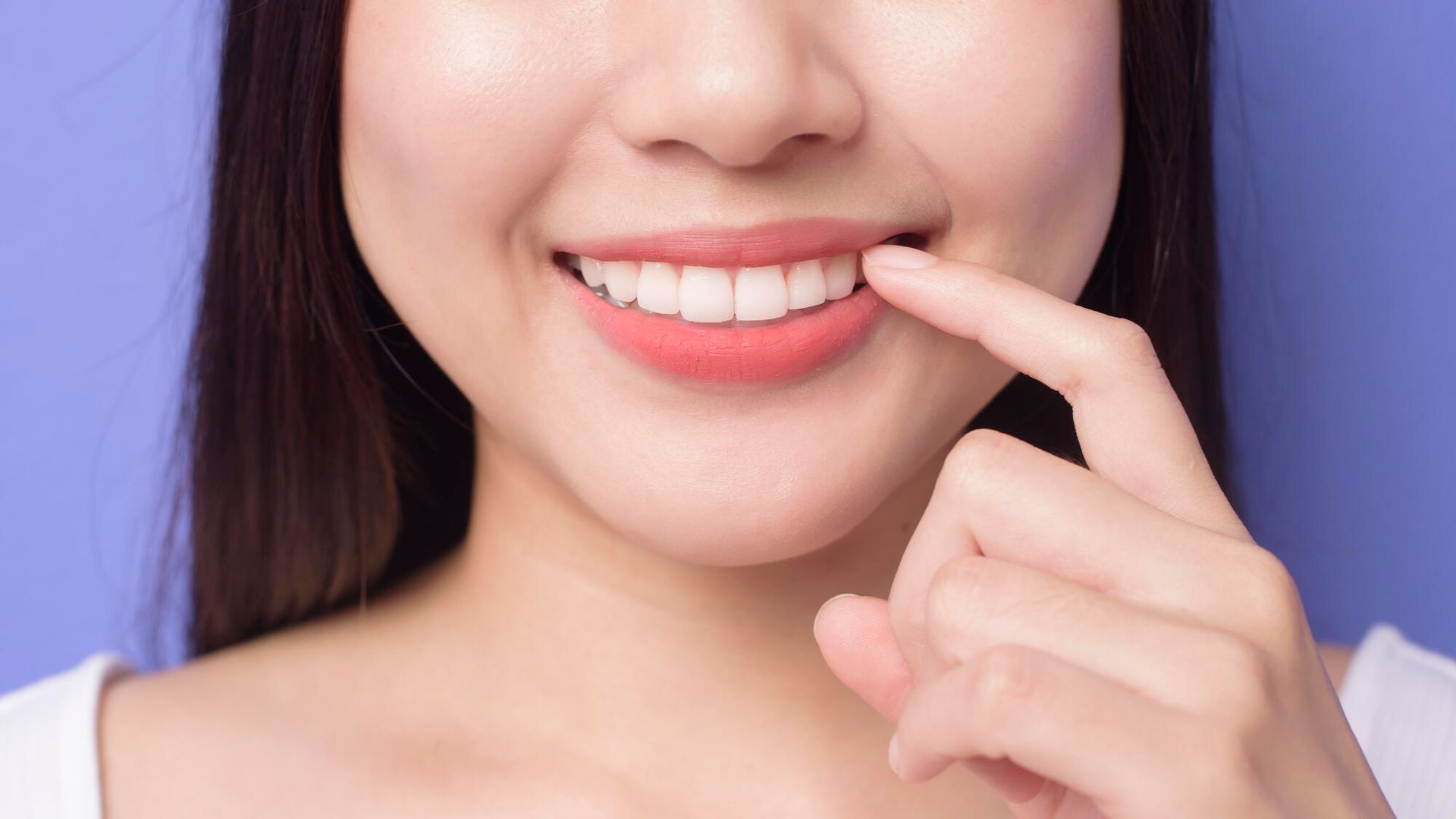 A woman is smiling and touching her teeth with her finger.