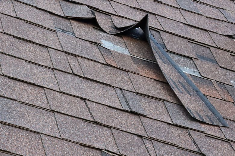 Damaged asphalt shingle roof with torn and missing sections.