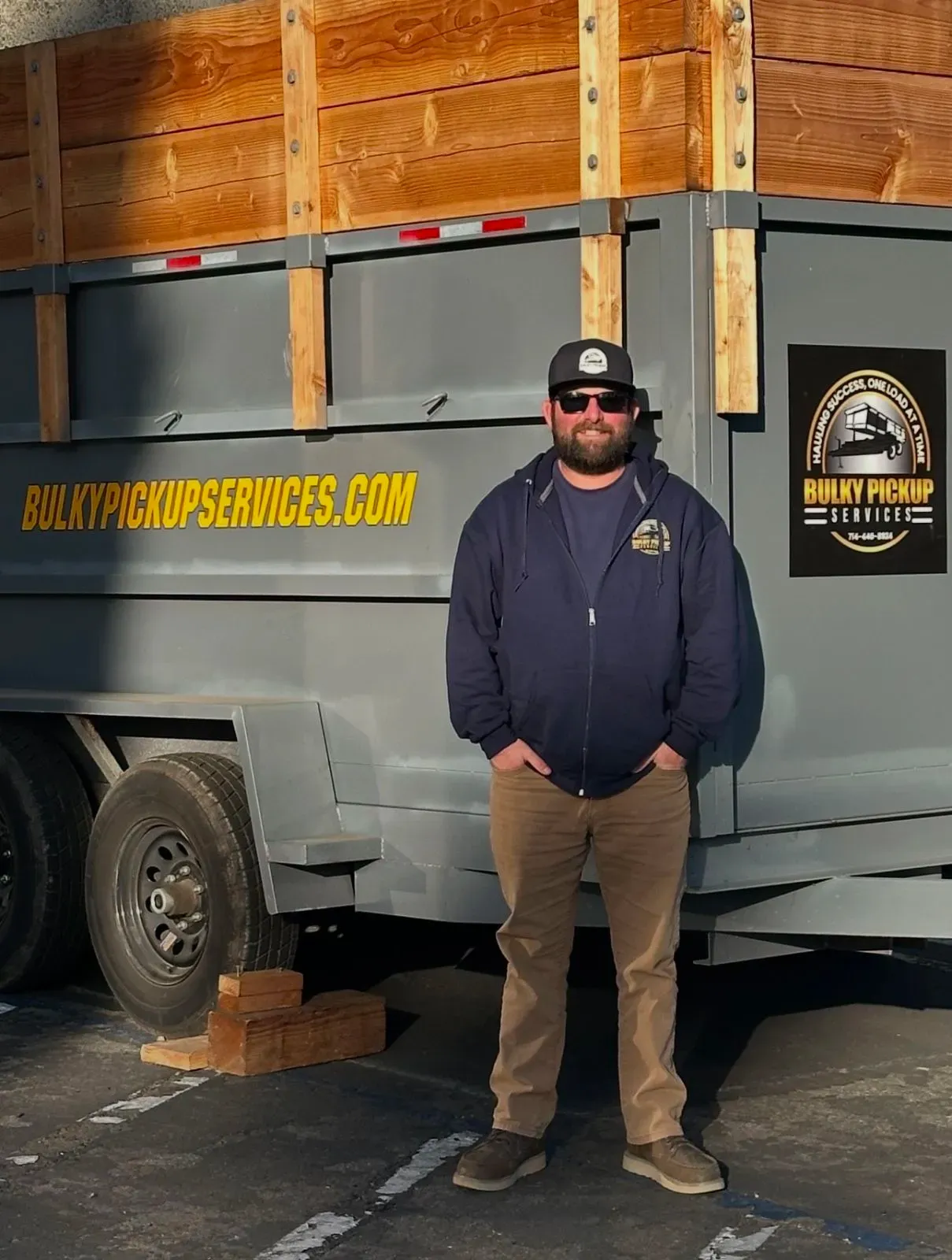 A man standing in front of a dumpster that says dump services.com