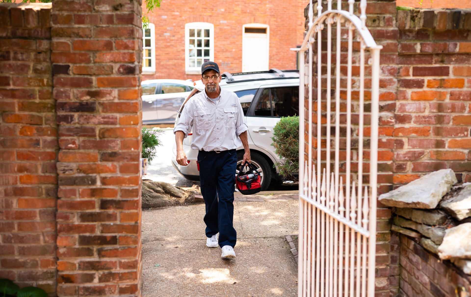 Man walking through a wrought iron gate with brick columns outdoors