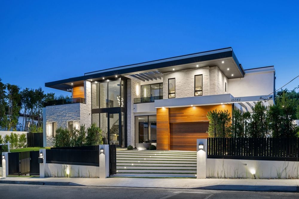 Modern two-story house with white brick exterior, wooden accents, and a large glass entryway at dusk.