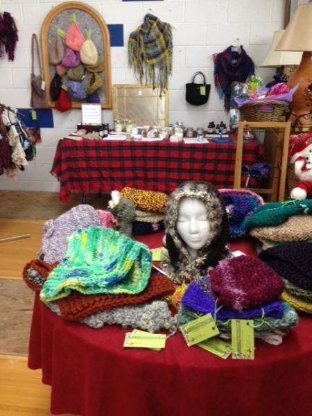 Craft market display of knitted hats, scarves, and colorful textiles on tables with a mannequin head