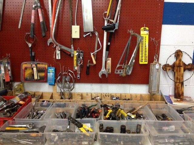 Tool wall with hanging hand tools and plastic bins of parts in a workshop.