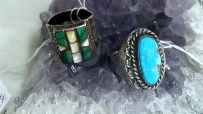 Two silver rings on amethyst crystals, one with green mosaic stones and one with a turquoise oval stone