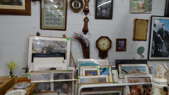 Wall of framed art, clocks, and shelves of books and framed prints in a cozy interior display.