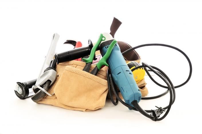 A tan tool bag filled with assorted hand tools and power cords on a white background