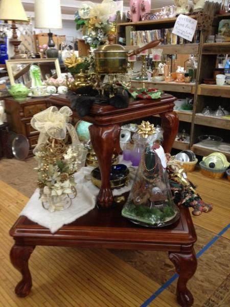 Antique wooden table with glass cloches and decorative figurines in a shop filled with vintage decor.