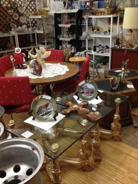 Antique shop display with red chairs, glass-topped table, figurines, and shelves of home decor