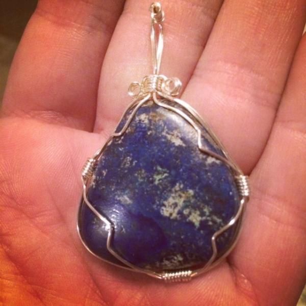 Wire-wrapped blue stone pendant with silver wire, held in a hand