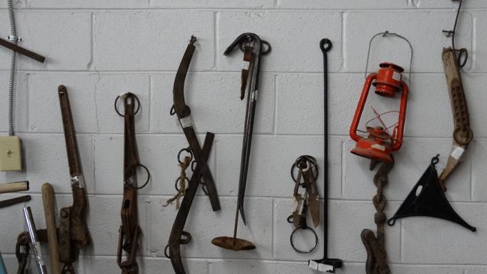 Collection of vintage hand tools and lanterns hanging on a white wall display