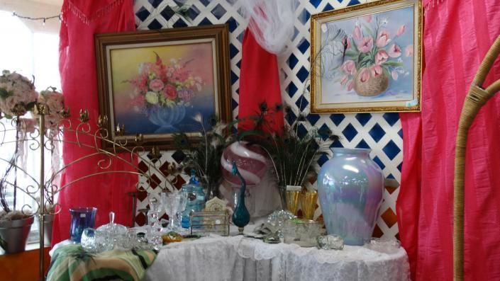 Decorative table display with floral paintings, vases, and lace against a red and white lattice backdrop