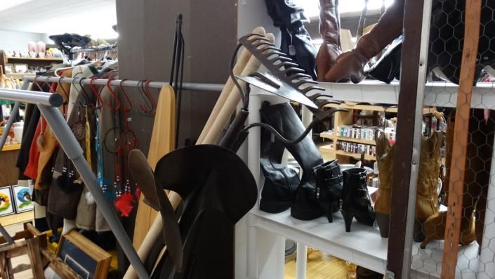 Cluttered thrift store aisle with clothing racks, shoes, and household items on shelves
