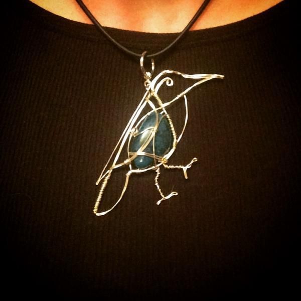 Silver wire bird pendant with a blue stone on a black cord necklace over a black top