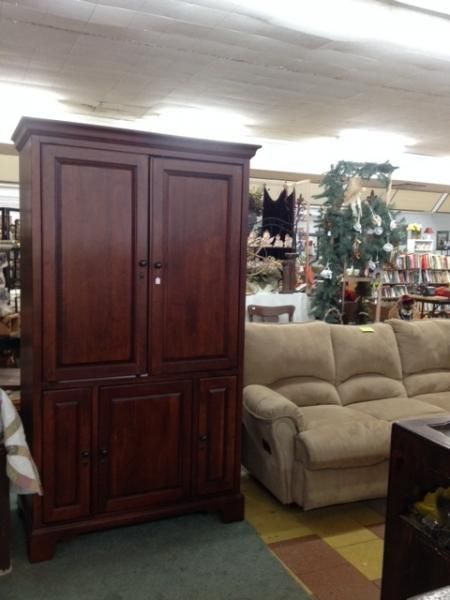 Furniture showroom with a dark wood cabinet beside a beige sofa and decorative greenery