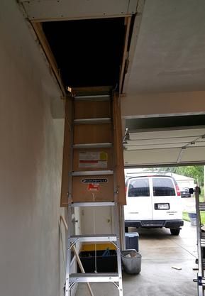 A ladder is going up to the attic in a garage.