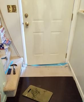 A white door is open in a hallway with a hammer and a mat on the floor.