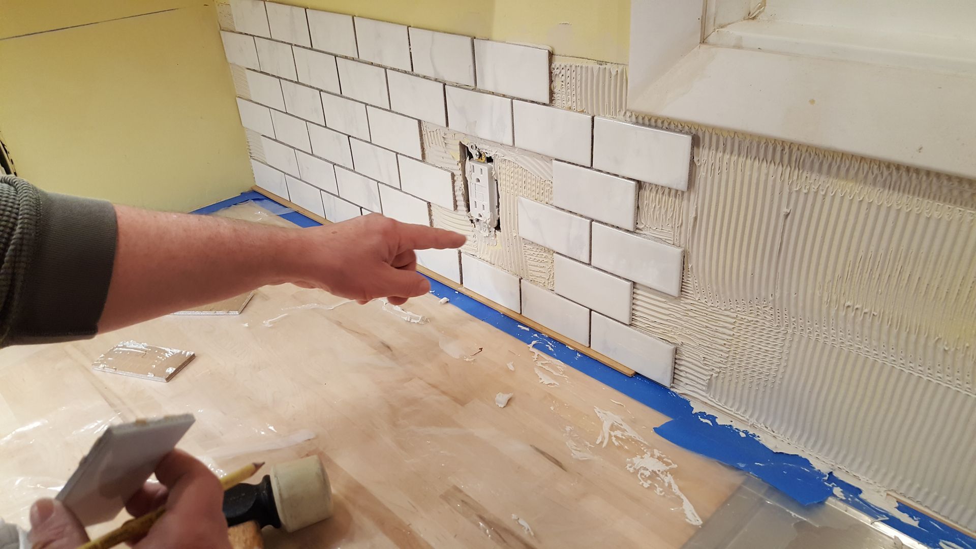 A person is pointing at a brick wall in a kitchen.