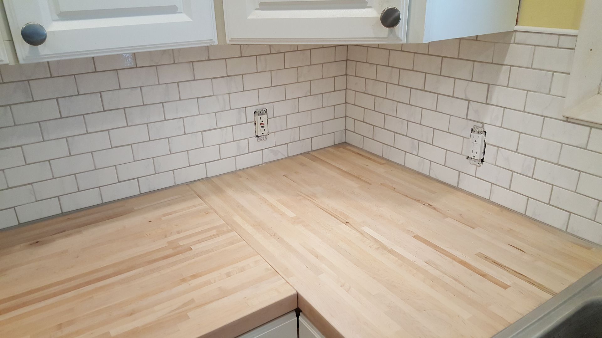 A kitchen with a wooden counter top and white subway tiles.