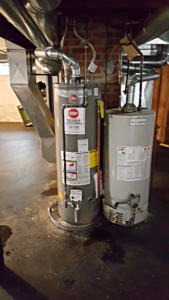 Two water heaters are sitting next to each other in a basement.