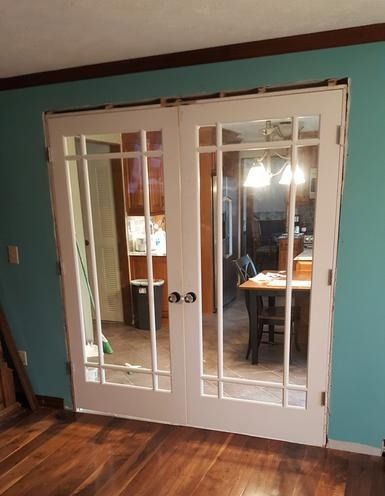 A living room with hardwood floors and french doors leading to a kitchen.