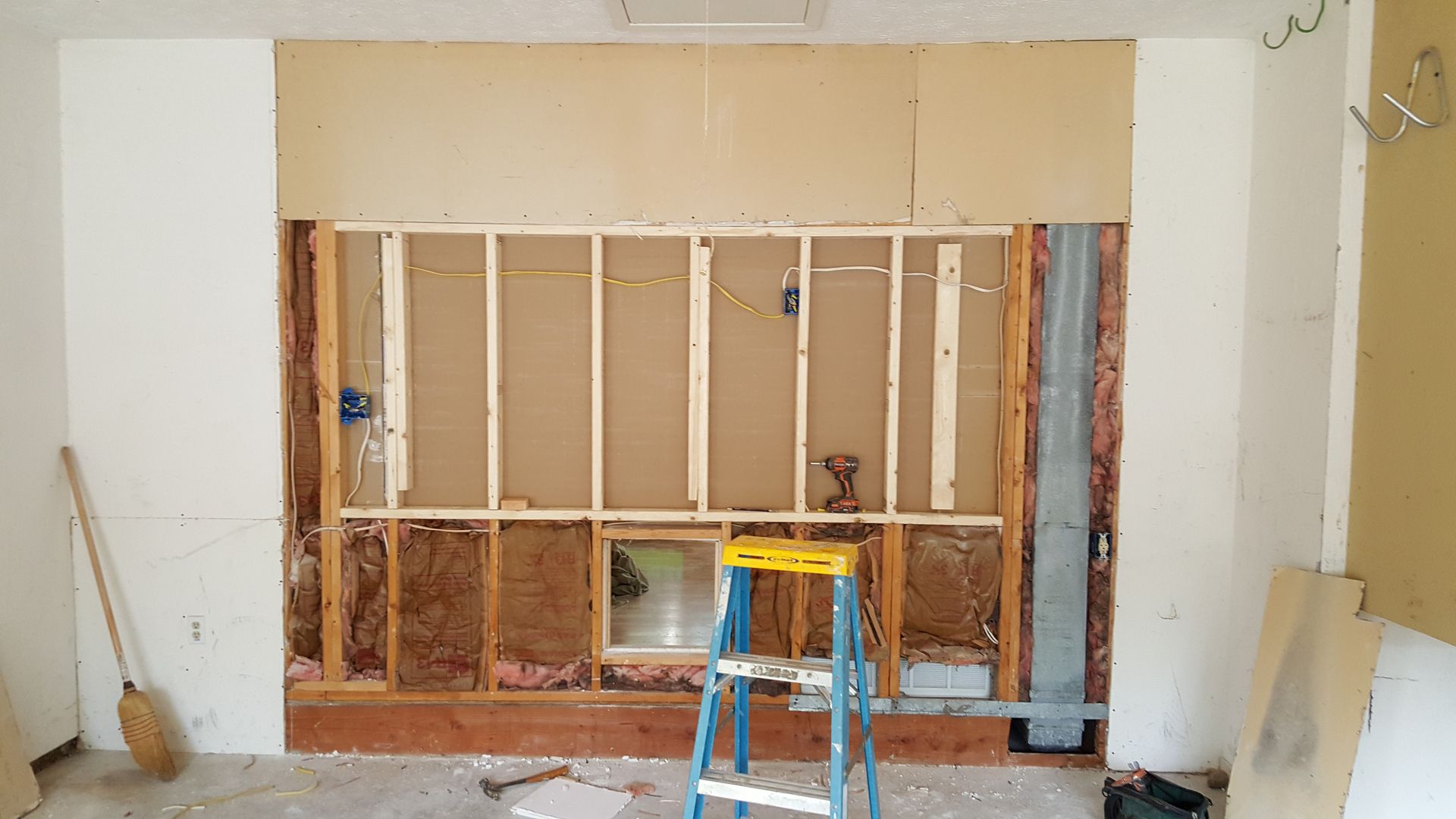 A ladder is sitting in front of a wall that is being remodeled.