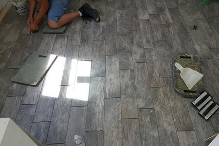 A man is laying tiles on the floor in a room.
