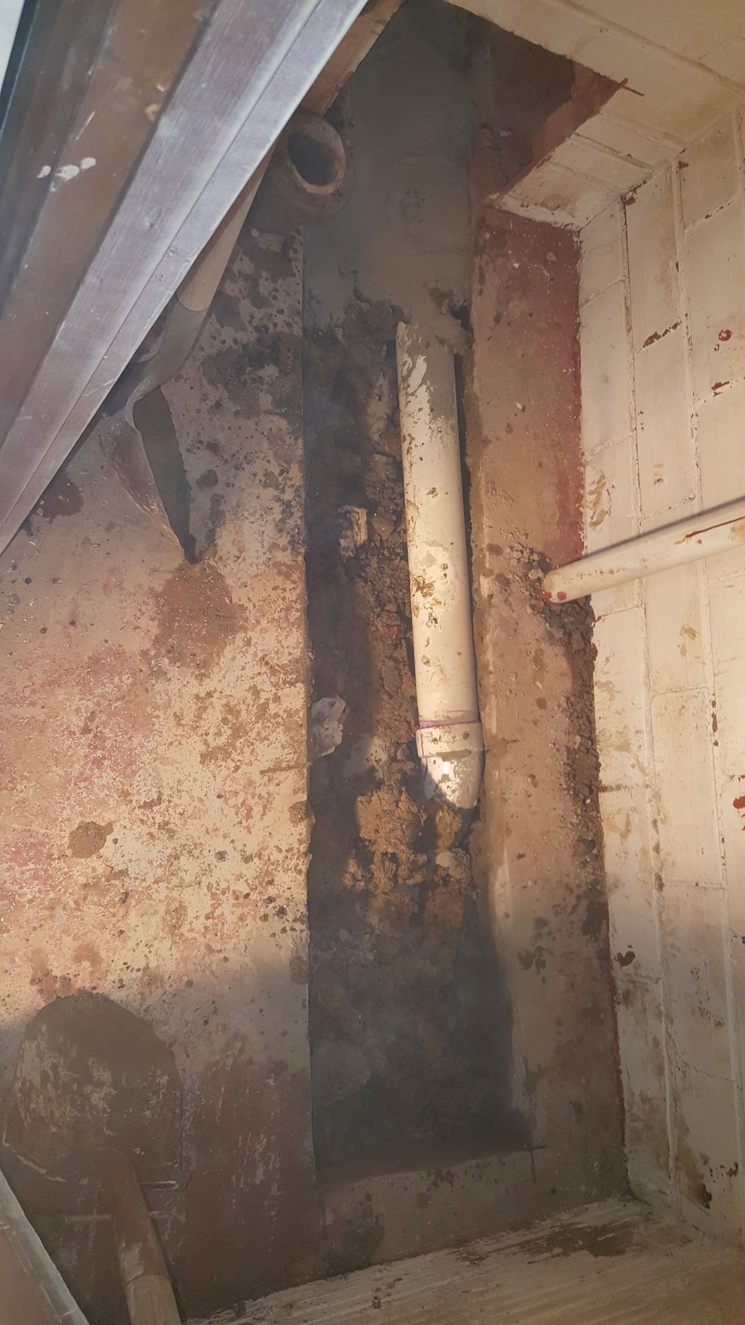 A white pipe is coming out of a hole in a wall.