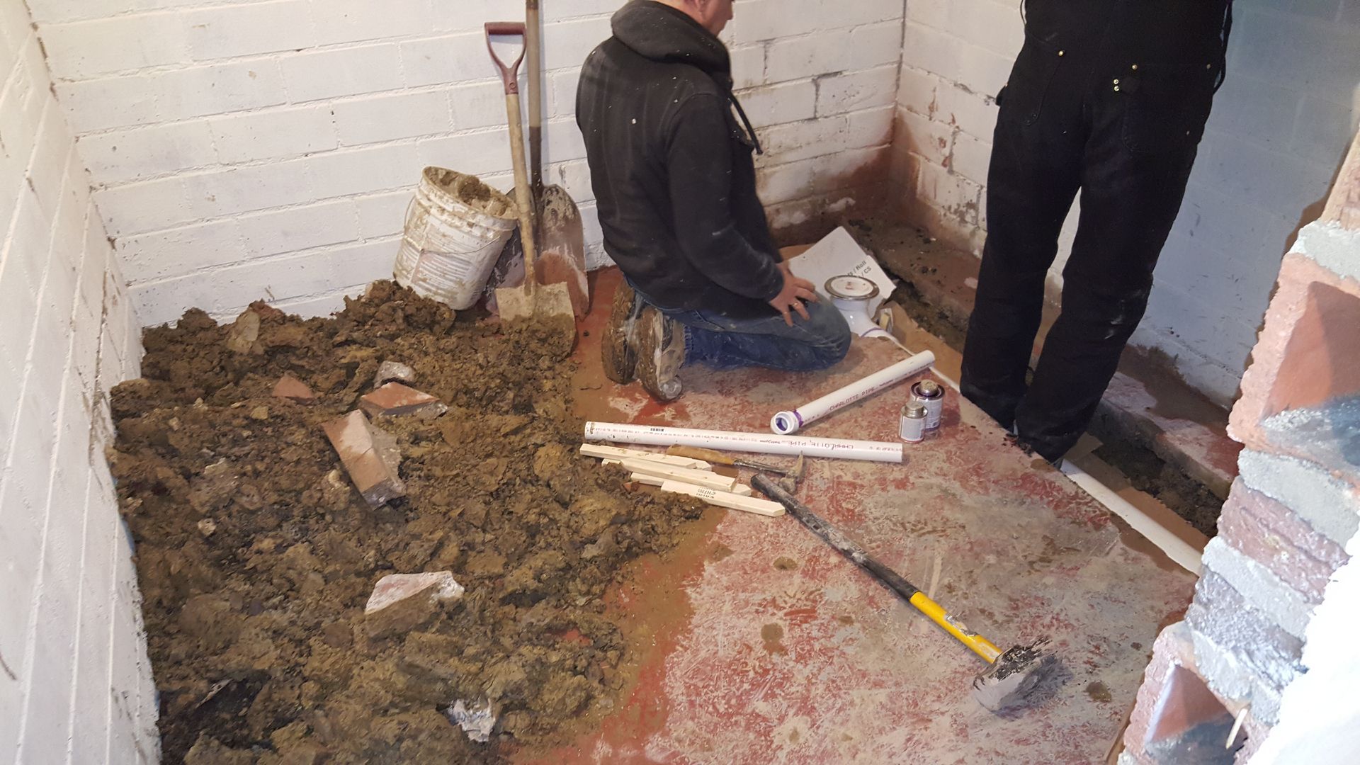A man is kneeling on the floor in a room with a shovel.