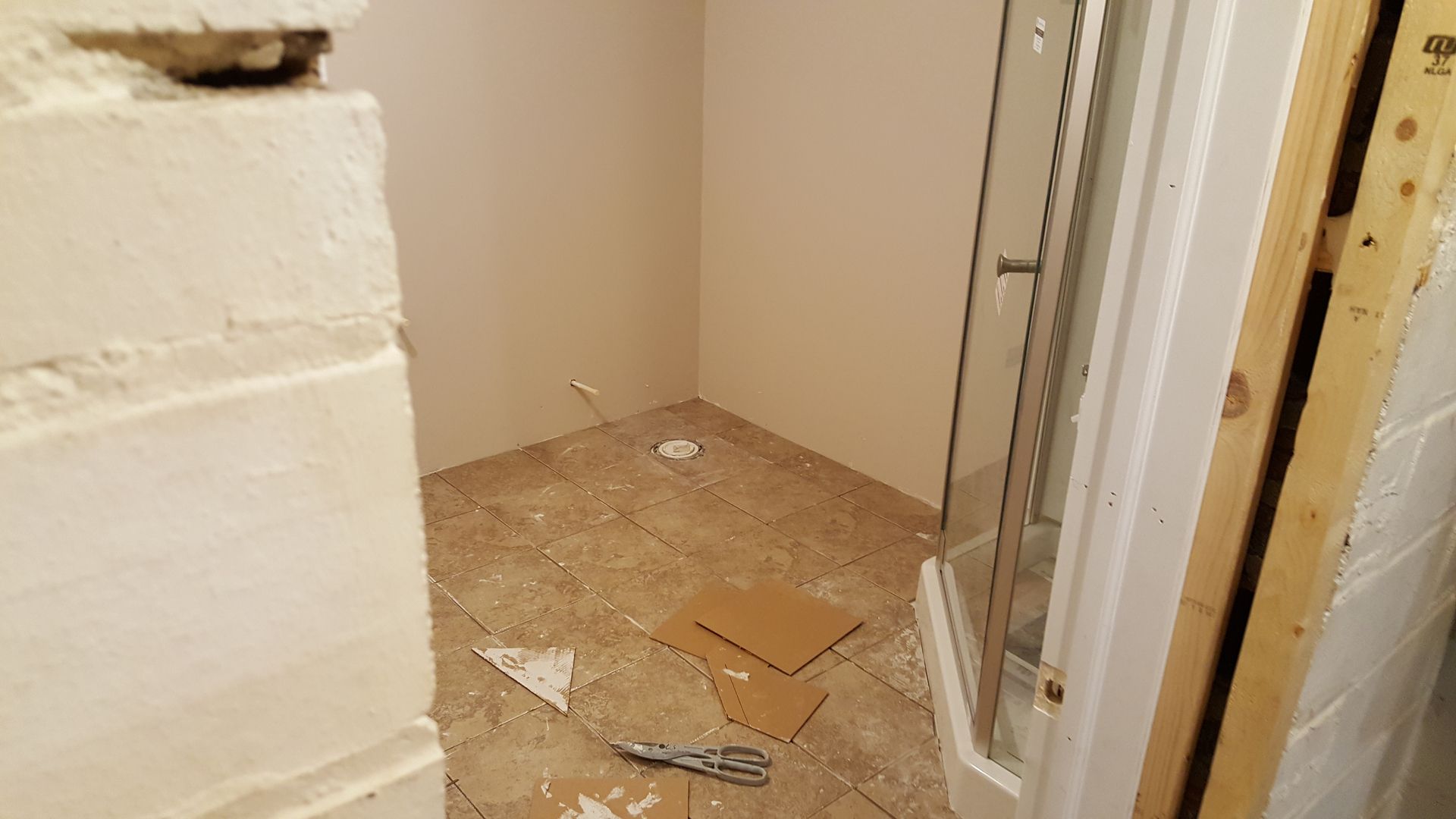 A bathroom with a shower stall and a pair of scissors on the floor.