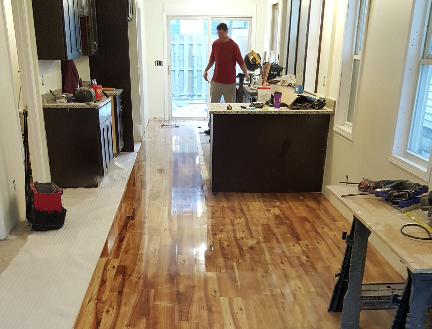 A man is standing in a kitchen with hardwood floors.