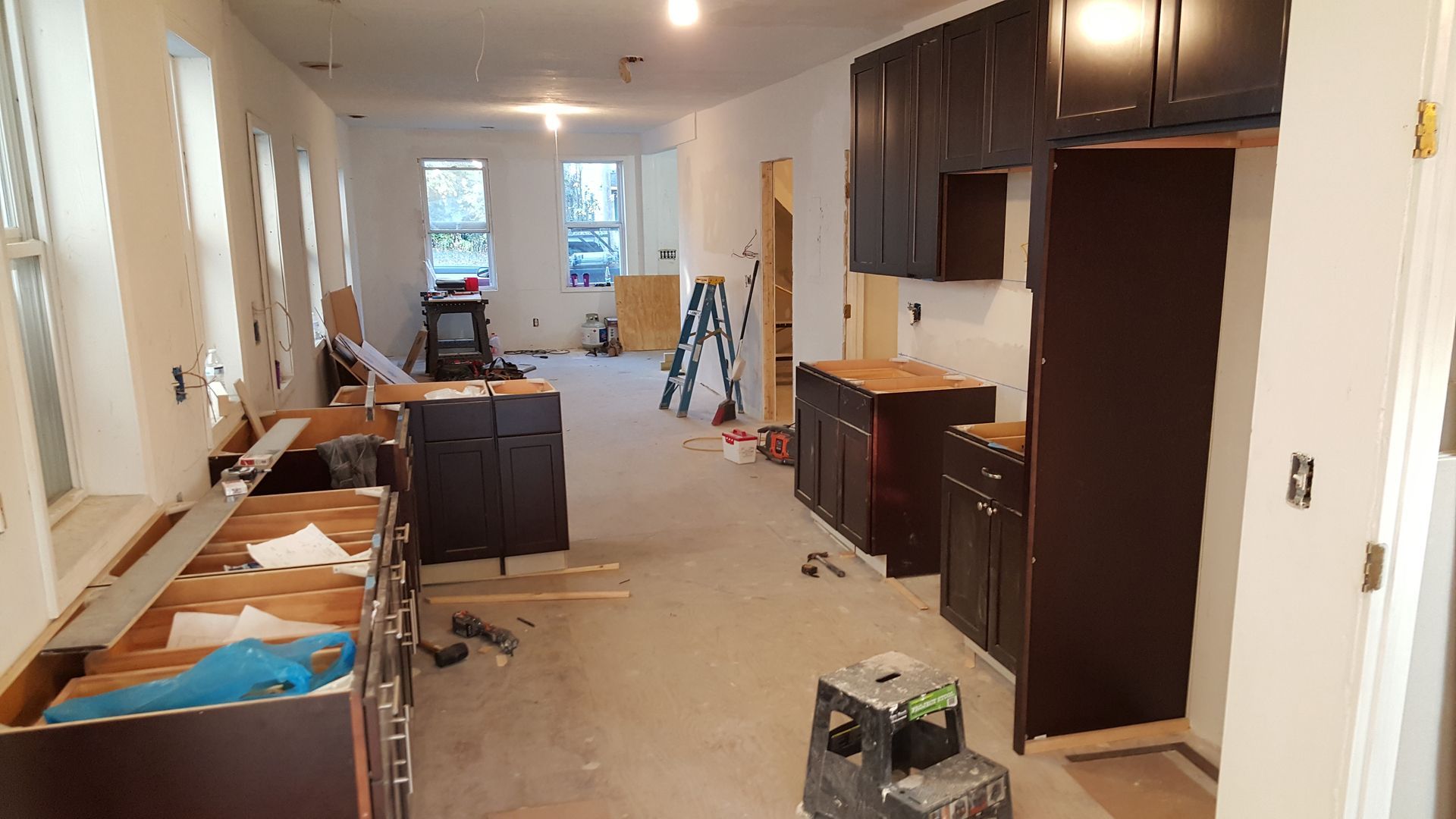 A kitchen under construction with black cabinets and a ladder.