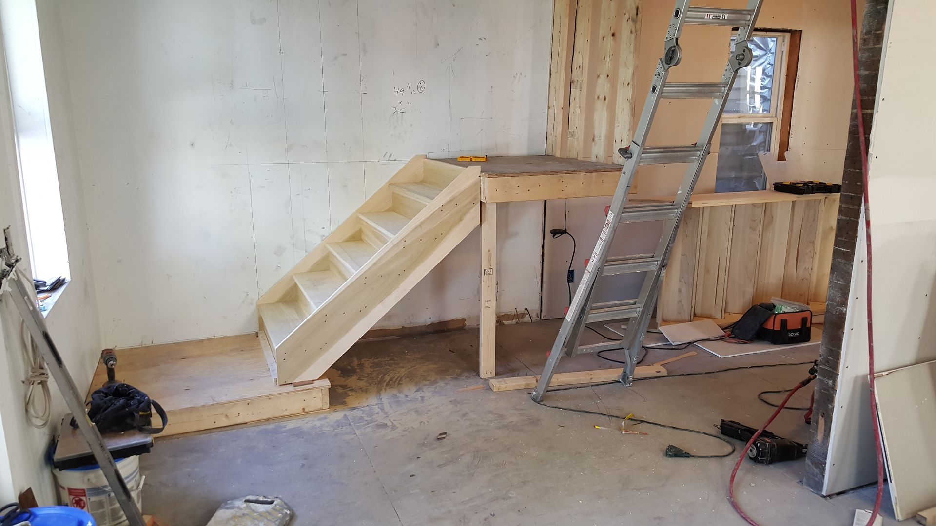A wooden staircase is being built in a room with a ladder.