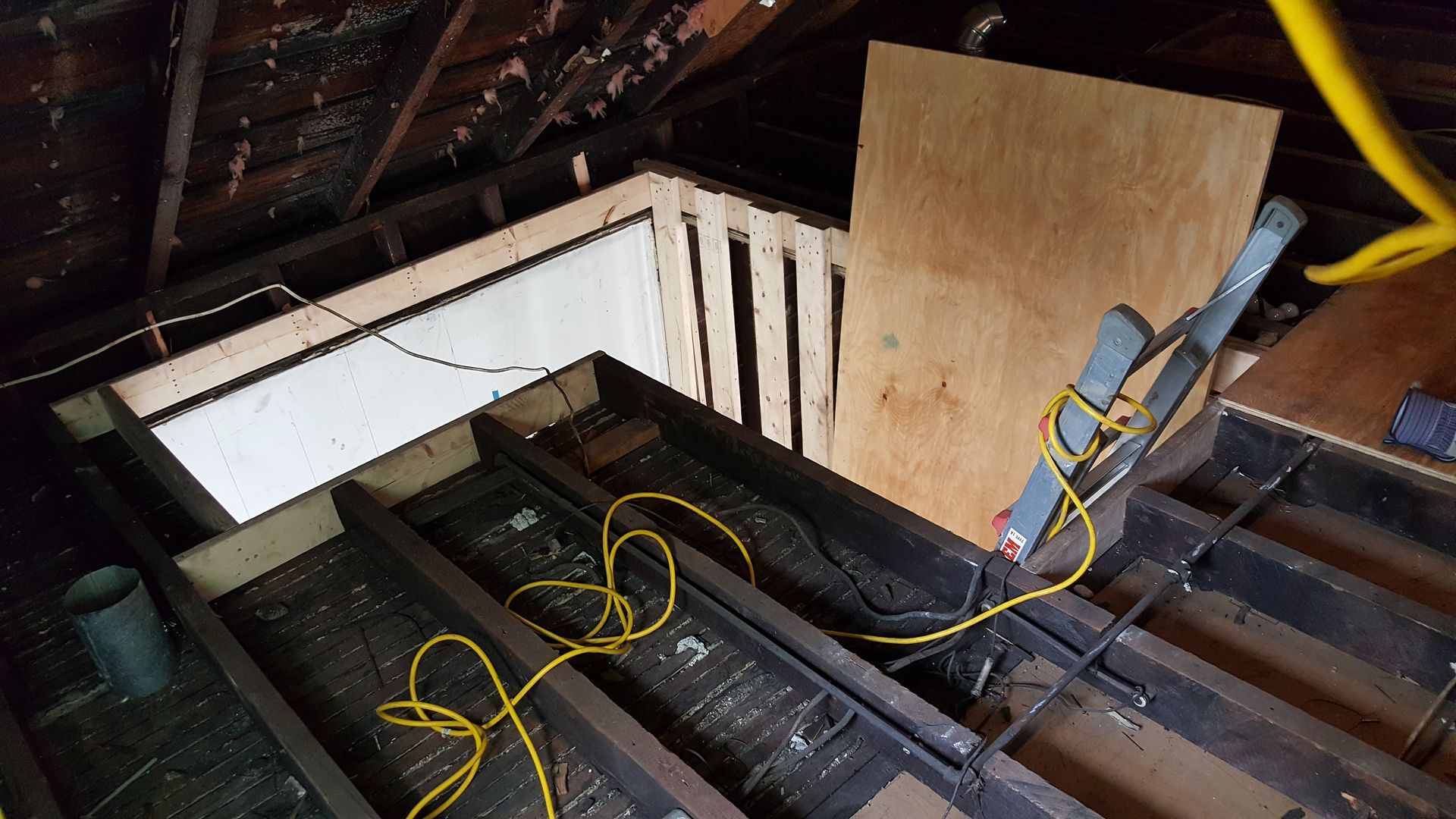 A ladder is sitting on top of a wooden floor in an attic.