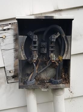 A dirty electrical box is sitting on the side of a house.