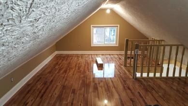 An empty attic with hardwood floors and a window.