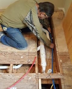 A man is kneeling on the floor fixing pipes.
