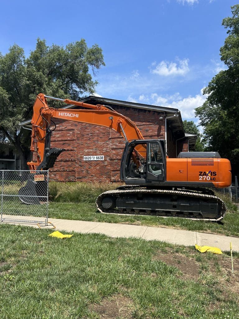 A large excavator is parked in front of a brick building.