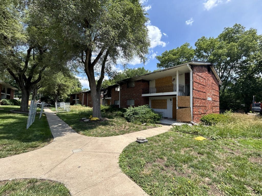 A brick apartment building with a sidewalk and trees in front of it.