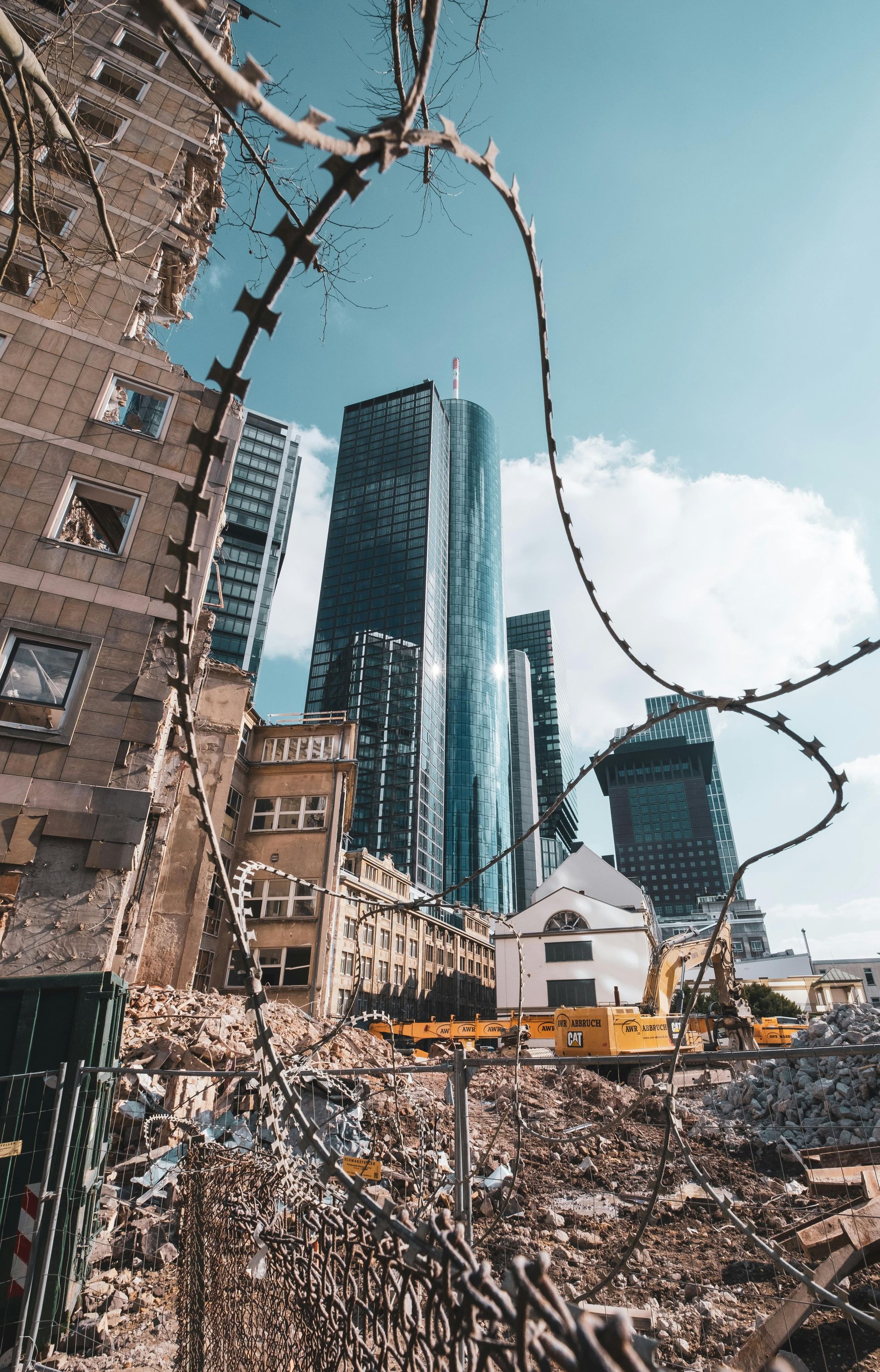 City buildings with construction; rubble in foreground, barbed wire, blue sky.