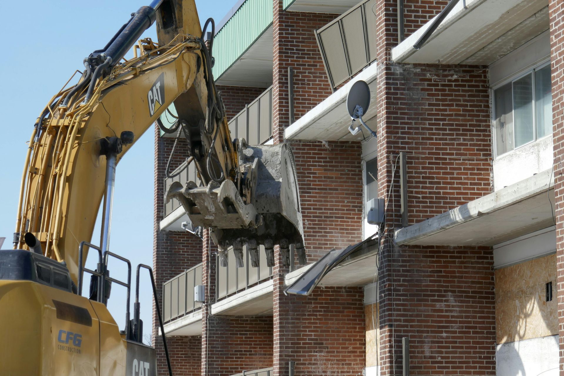 Excavator demolishing a brick apartment building balcony beside a staircase