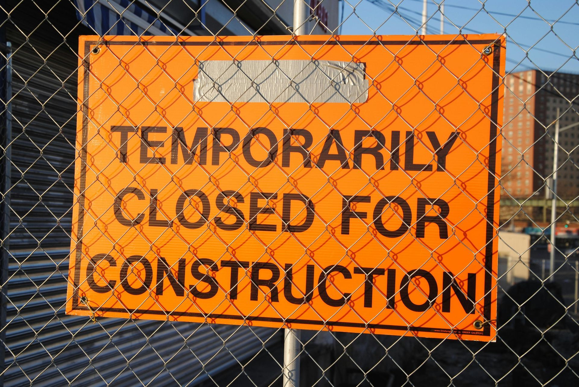 An orange sign on a chain link fence says temporarily closed for construction