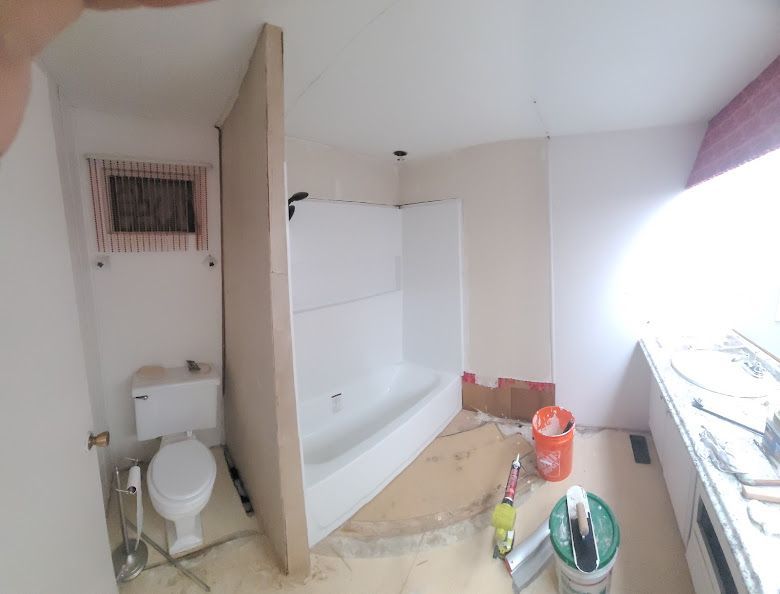 Bathroom renovation: Toilet, shower/tub combo, partial wall. Beige walls, white fixtures, supplies on floor.