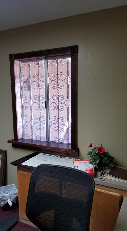 A window with decorative bars, a desk with chair, and a small keyboard sit in an office.