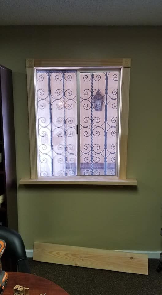Window with security bars, wood trim, on a green wall. Boards on the floor below.
