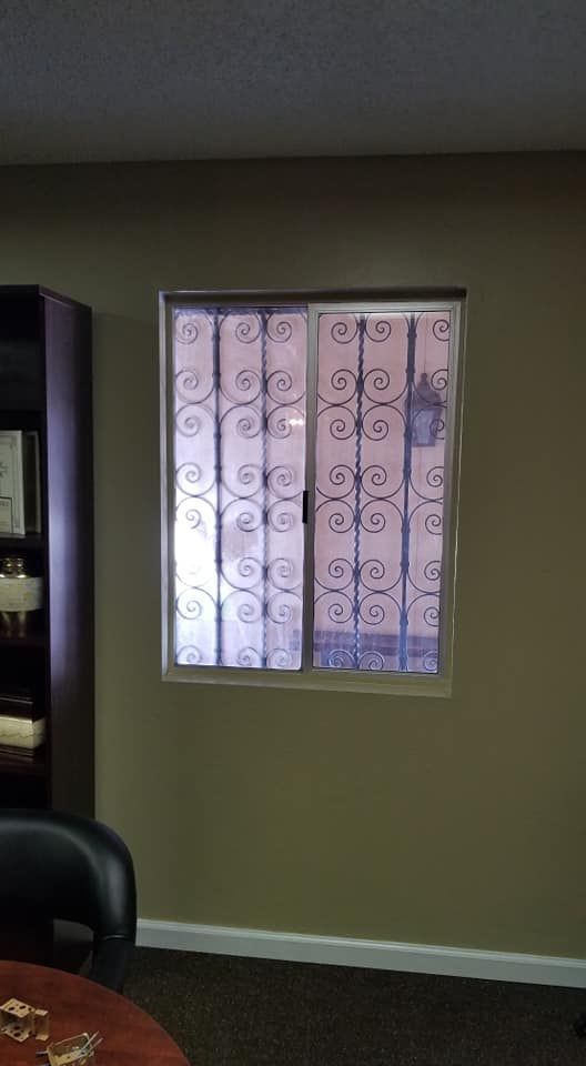 Window with ornate iron security bars, set in a green wall. Beside a dark wooden cabinet and a partial view of a desk.