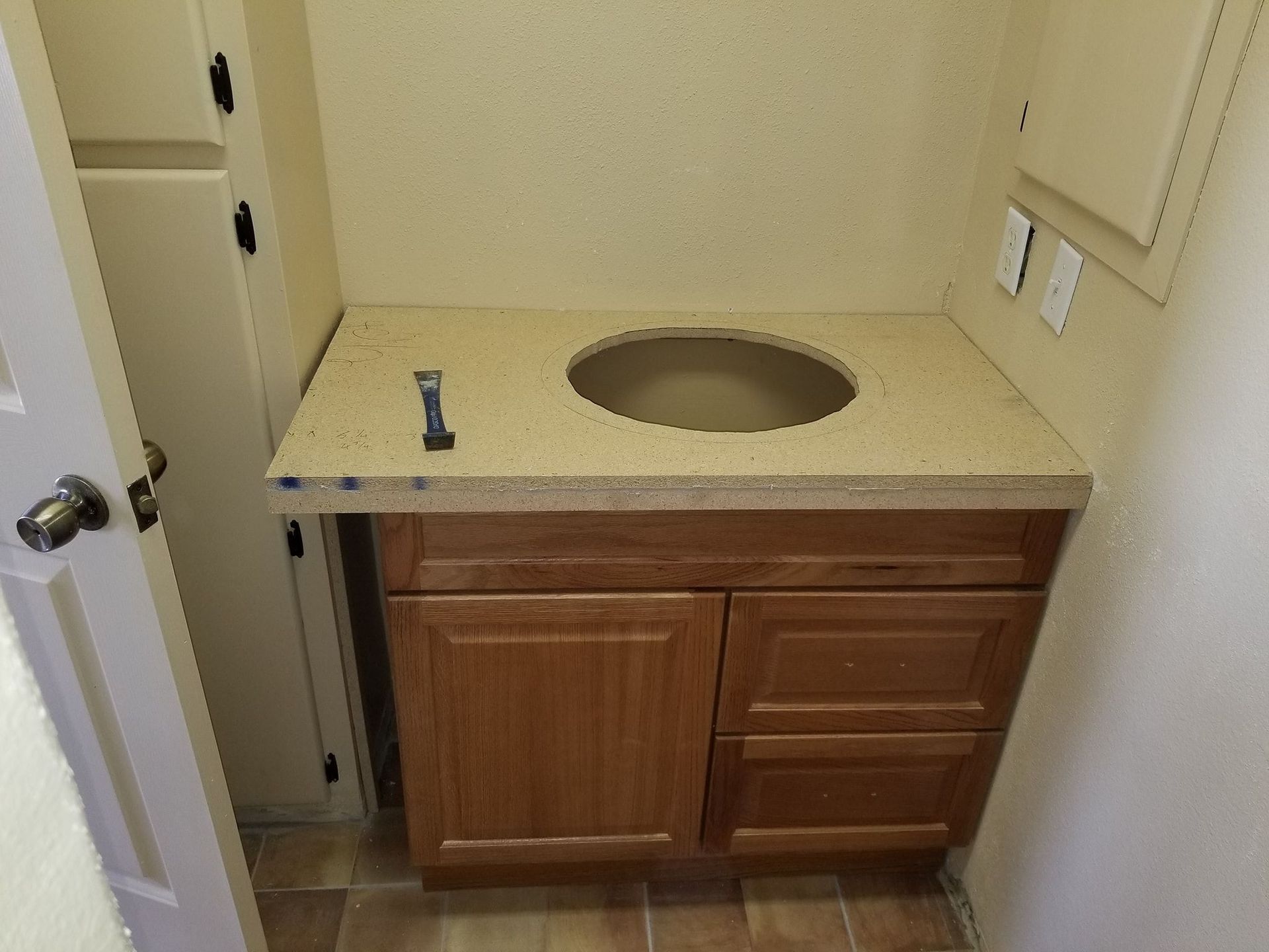 Bathroom vanity with brown cabinets and a beige countertop; round sink cutout.
