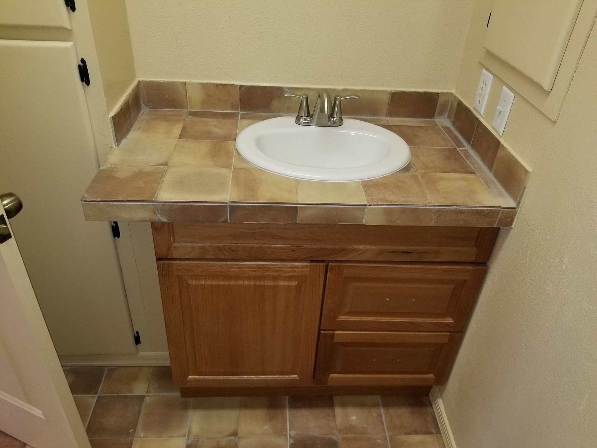 Bathroom vanity with a white sink, brown tiled countertop, and wood cabinet.
