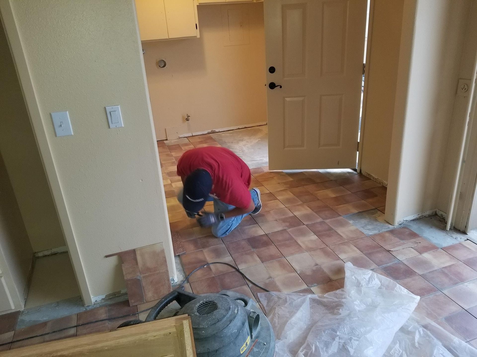 Man laying brick-style floor tiles indoors, kneeling. 