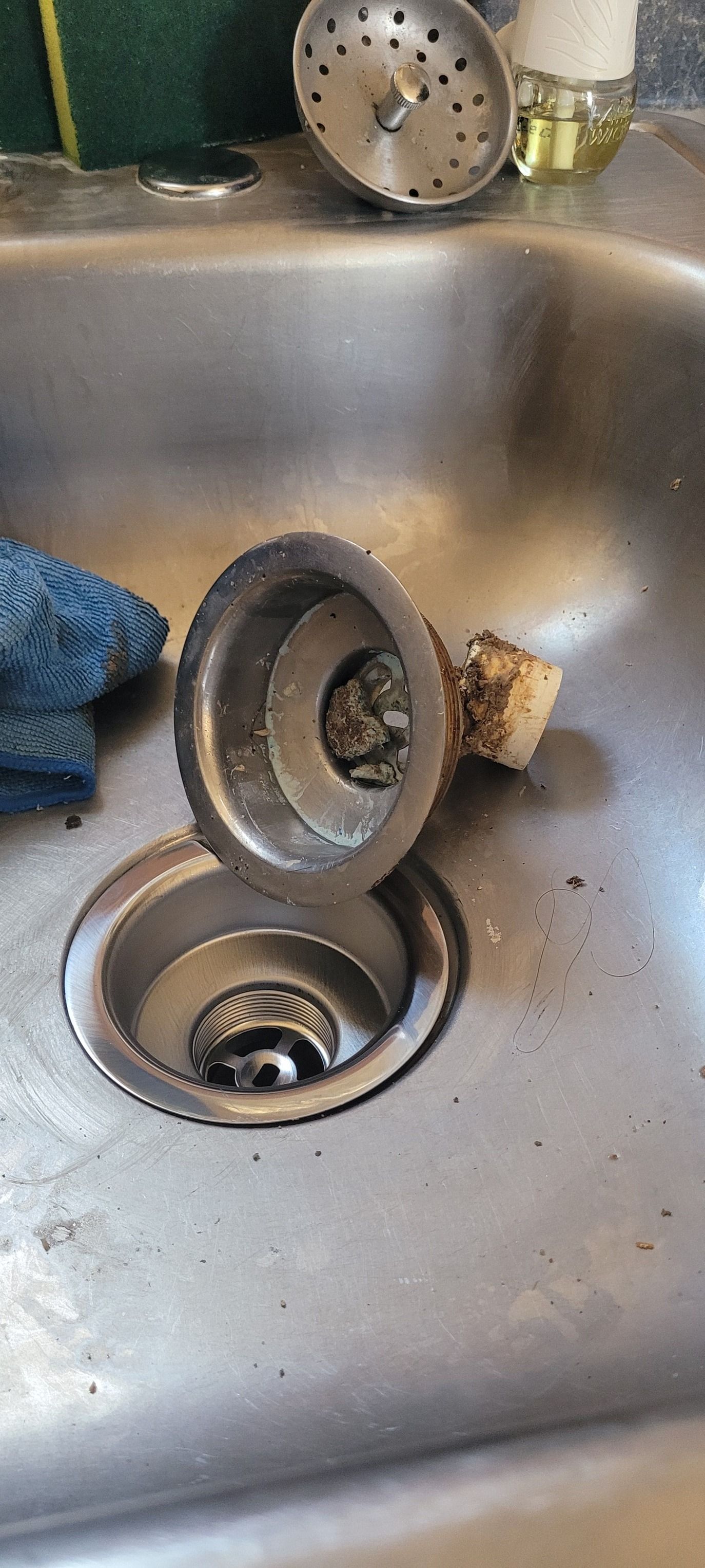 A stainless steel kitchen sink with a disassembled sink strainer, showing debris.